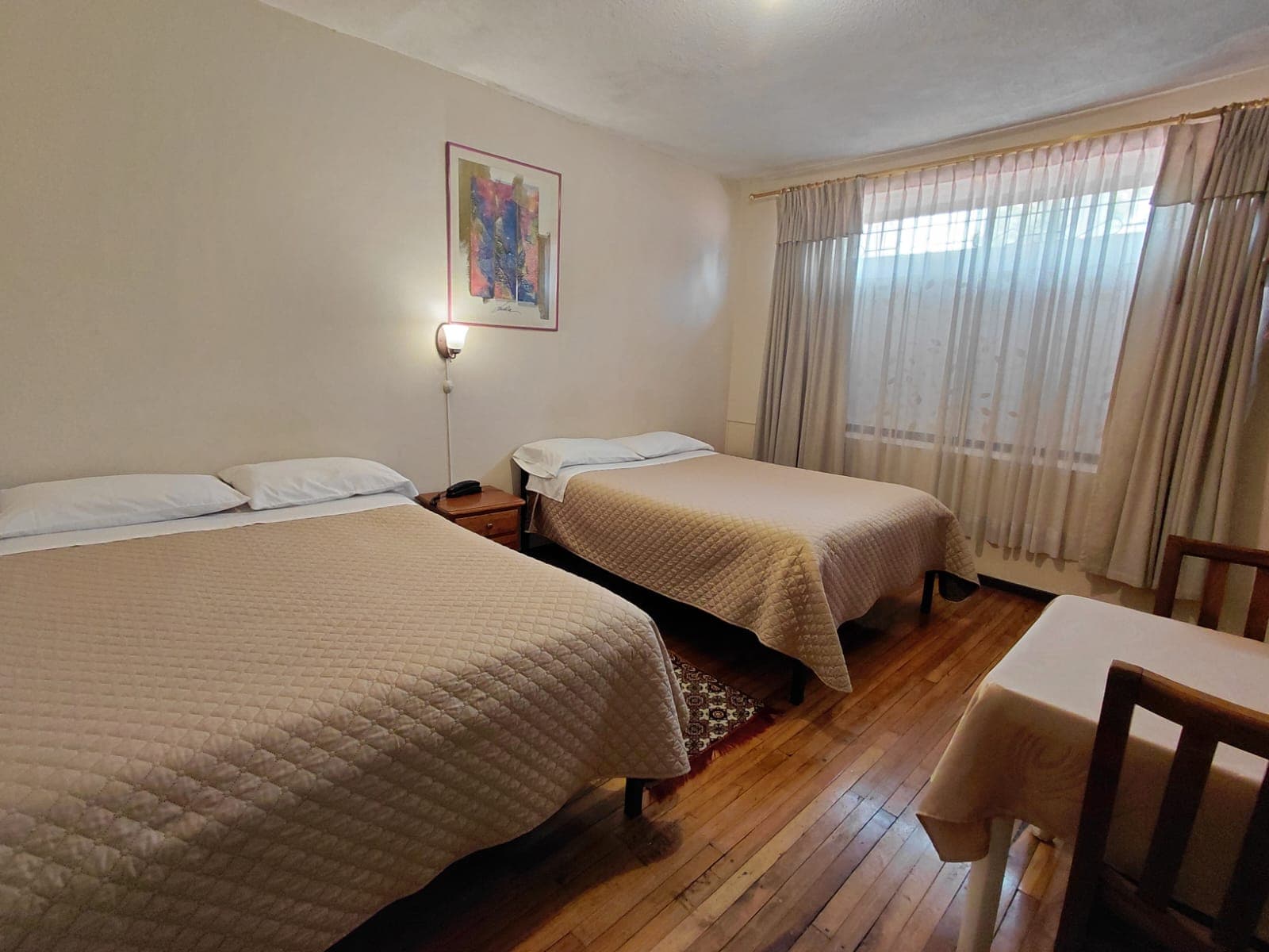 Habitación doble amplia con piso de madera y decoración cálida en hostal Quito