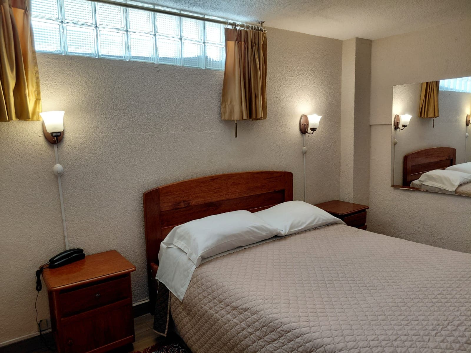 Habitación con cama doble, espejo y lámparas de lectura en hostal de Quito