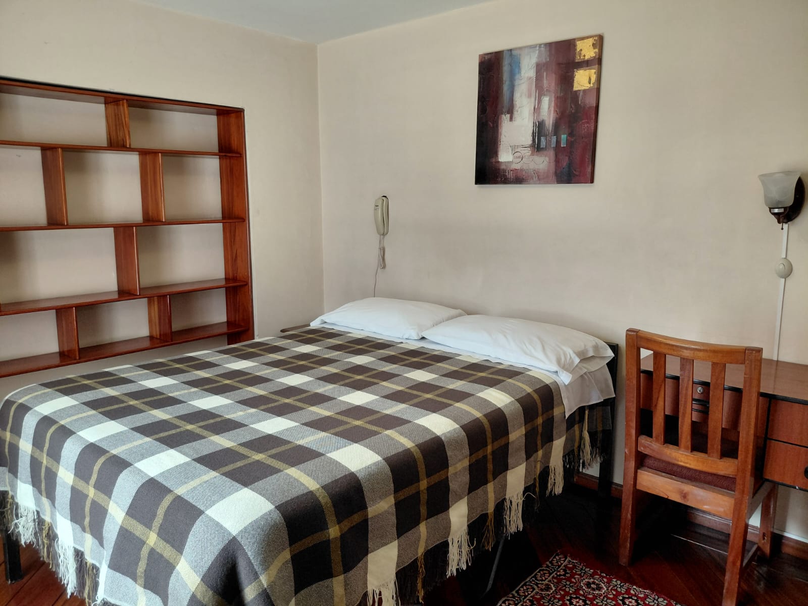 Habitación simple con cama doble, estantería de madera y escritorio en hostal Quito