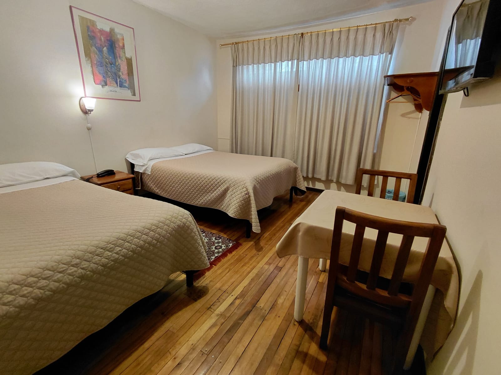 Habitación doble con dos camas, piso de madera y TV en hostal de Quito