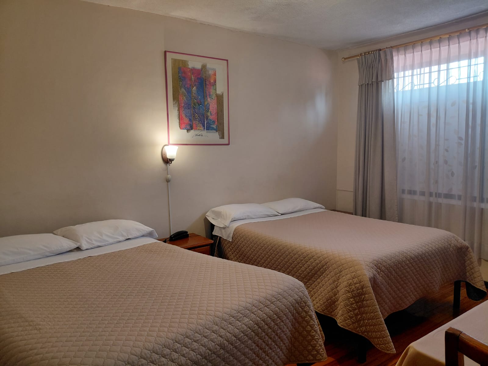 Habitación doble con dos camas y ventana amplia con cortinas en hostal de Quito