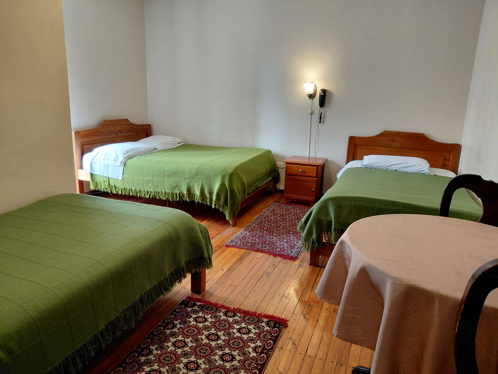 Habitación triple con tres camas, ropa de cama verde y piso de madera en hostal Quito