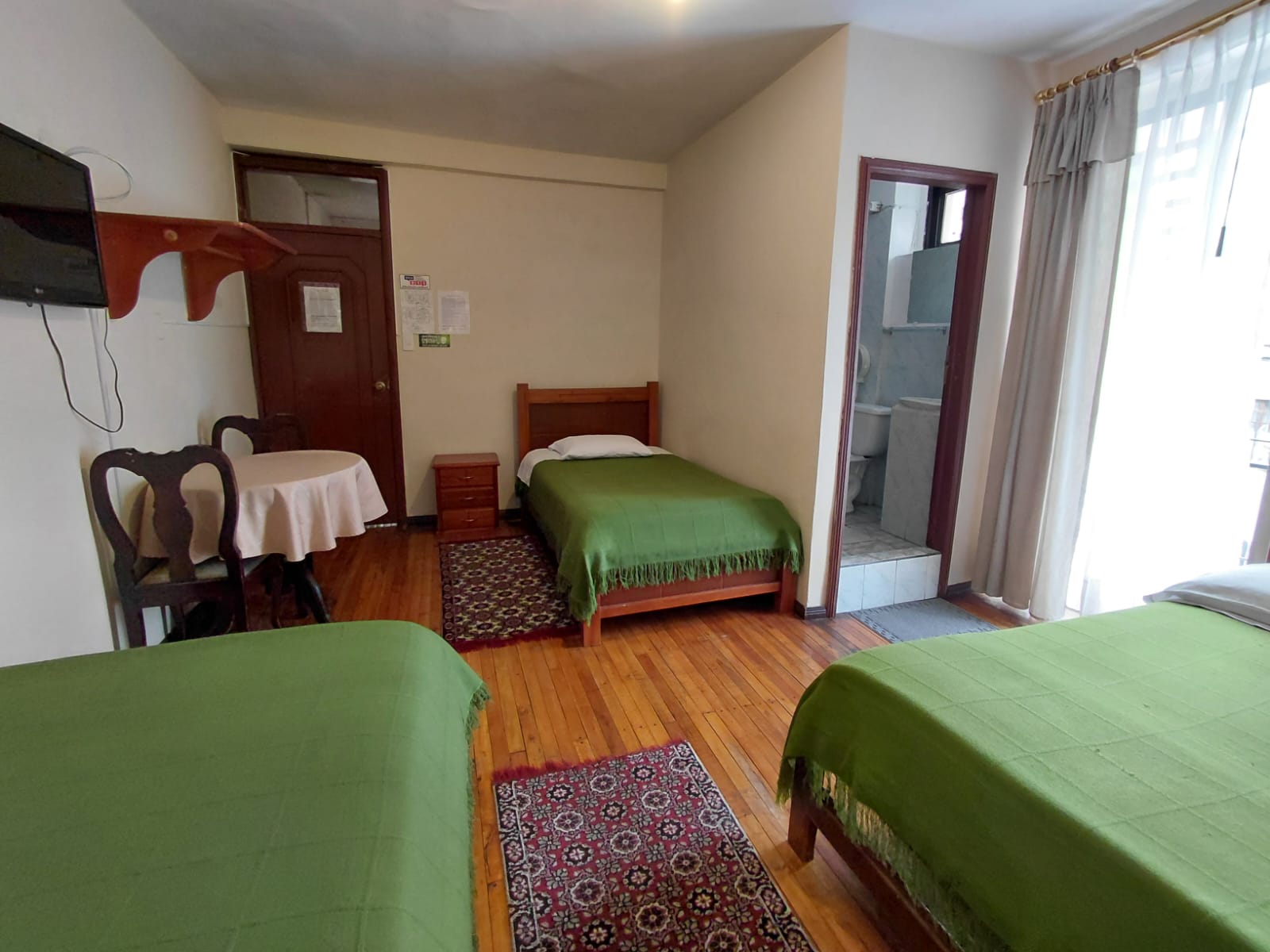 Habitación triple amplia con baño privado, TV y balcón en hostal de Quito