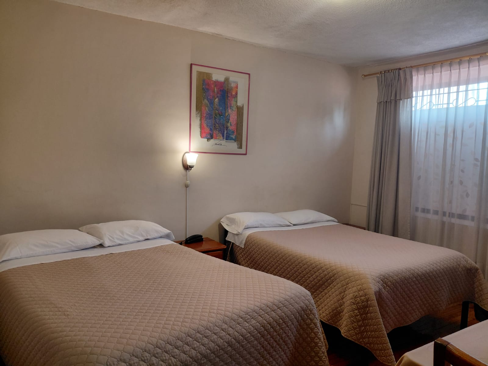 Habitación con dos camas, cuadro decorativo y lámpara de pared en hostal Quito