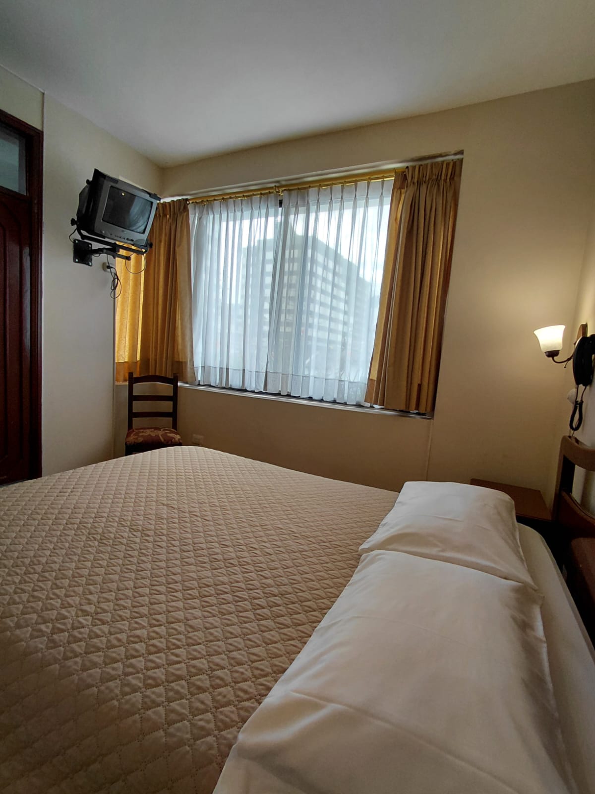 Habitación con cama doble, televisor y ventana amplia en hostal de Quito