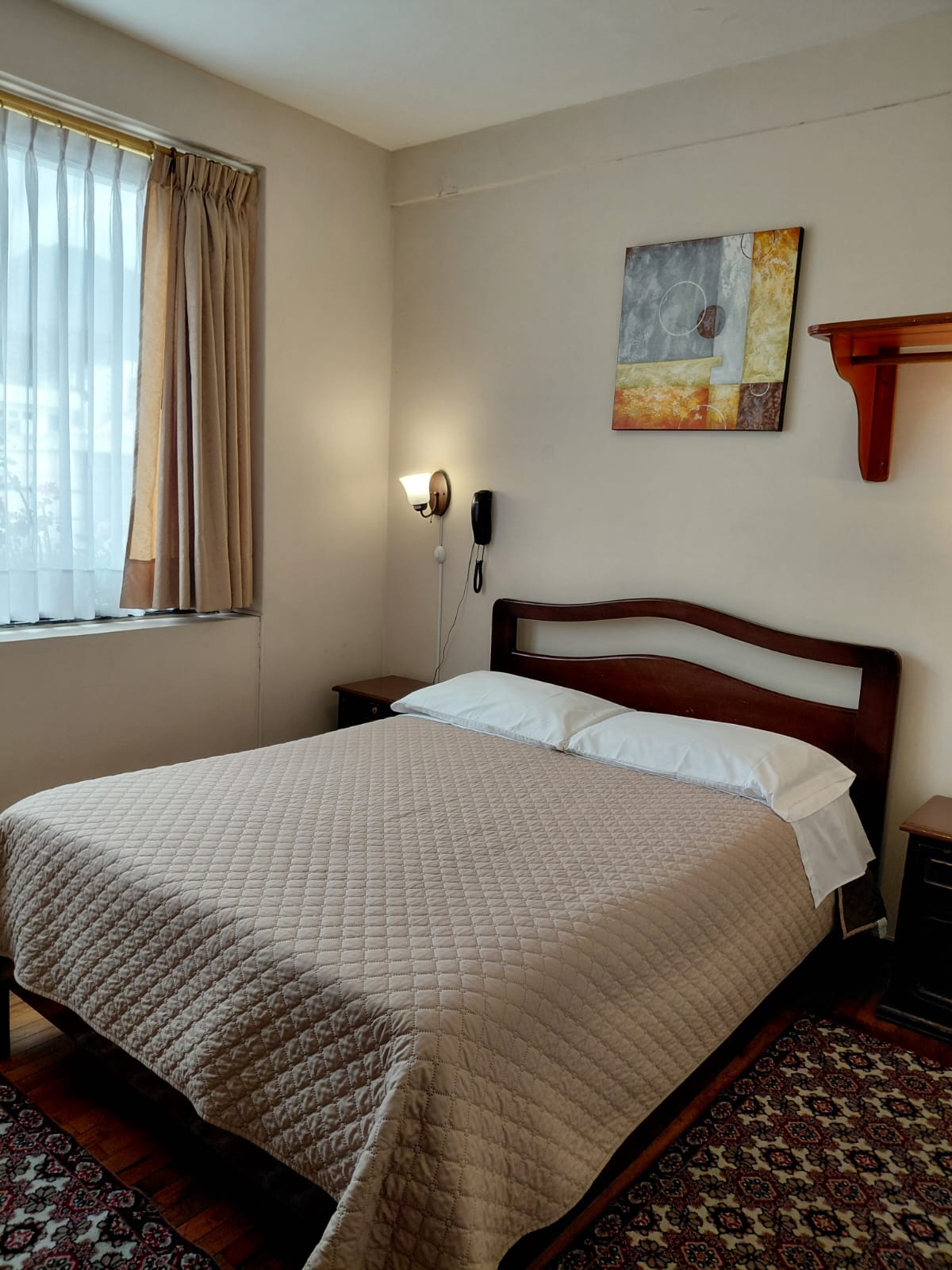 Habitación con cama doble, cuadro decorativo y alfombra persa en hostal de Quito