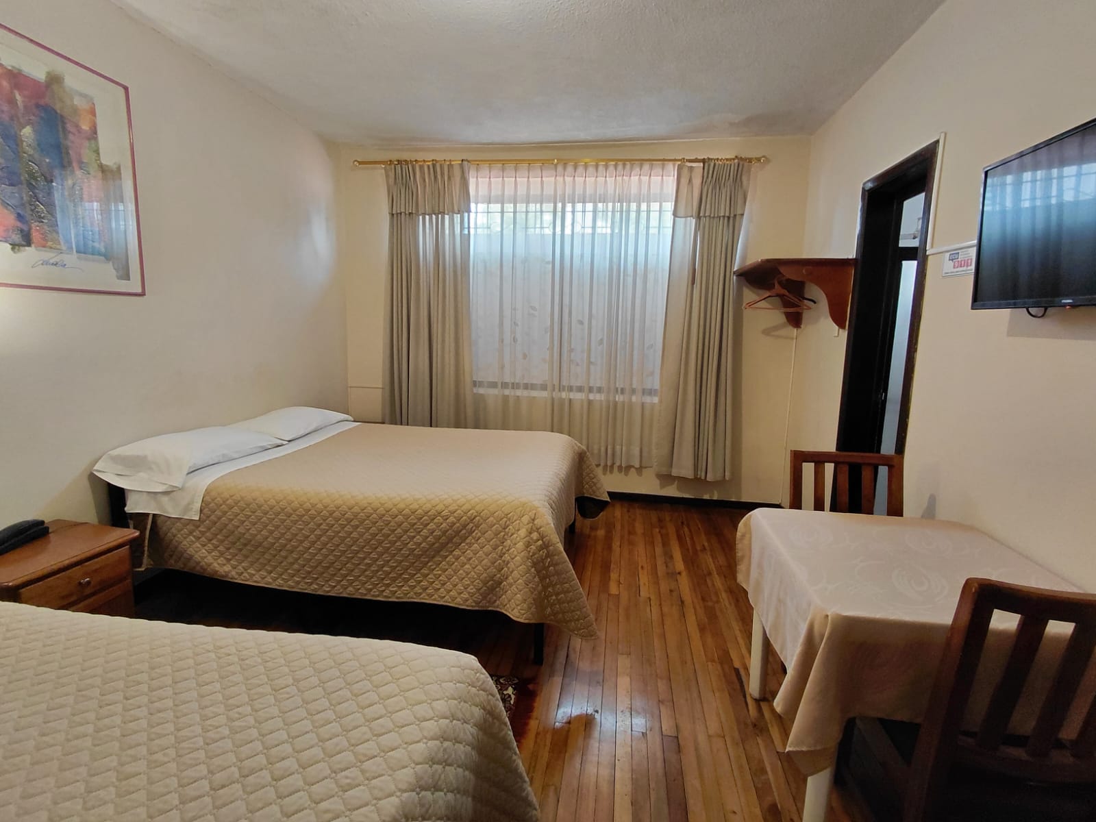 Habitación doble amplia con dos camas, TV y escritorio en hostal de Quito