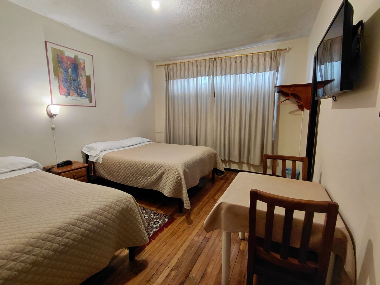 Habitación doble con dos camas, televisión y mobiliario de madera en hostal Quito