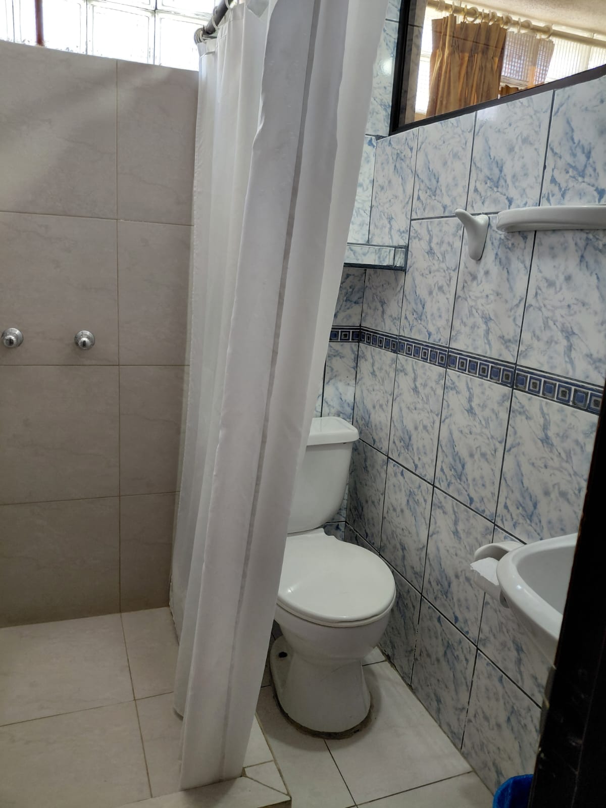 Baño con ducha de agua caliente y azulejos decorativos en hostal de Quito