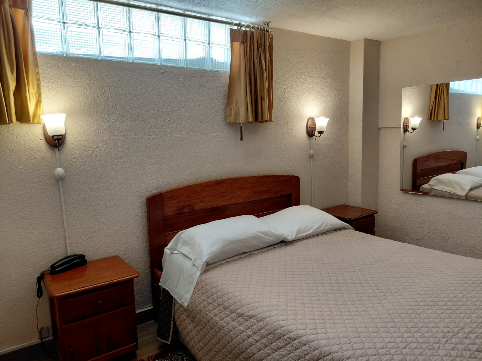 Habitación con cama doble, espejo y lámparas de lectura en hostal de Quito